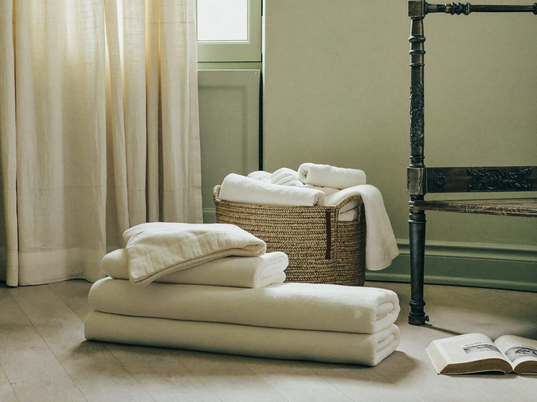 Linge de maison blanc plié dans un panier tressé, serviettes roulées à côté