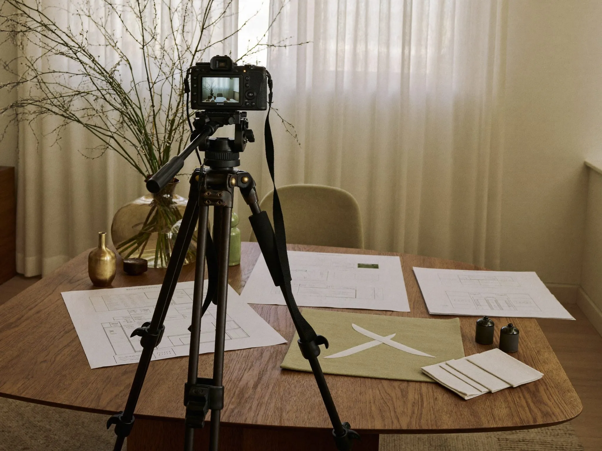 Appareil photo sur trépied face à un intérieur préparé, plans et échantillons de tissu sur une table de chêne