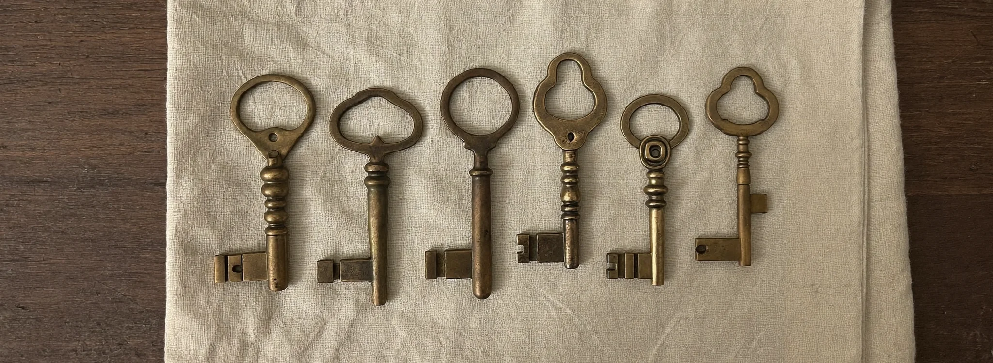 Six clés anciennes en laiton alignées sur du lin plié, lumière rasante