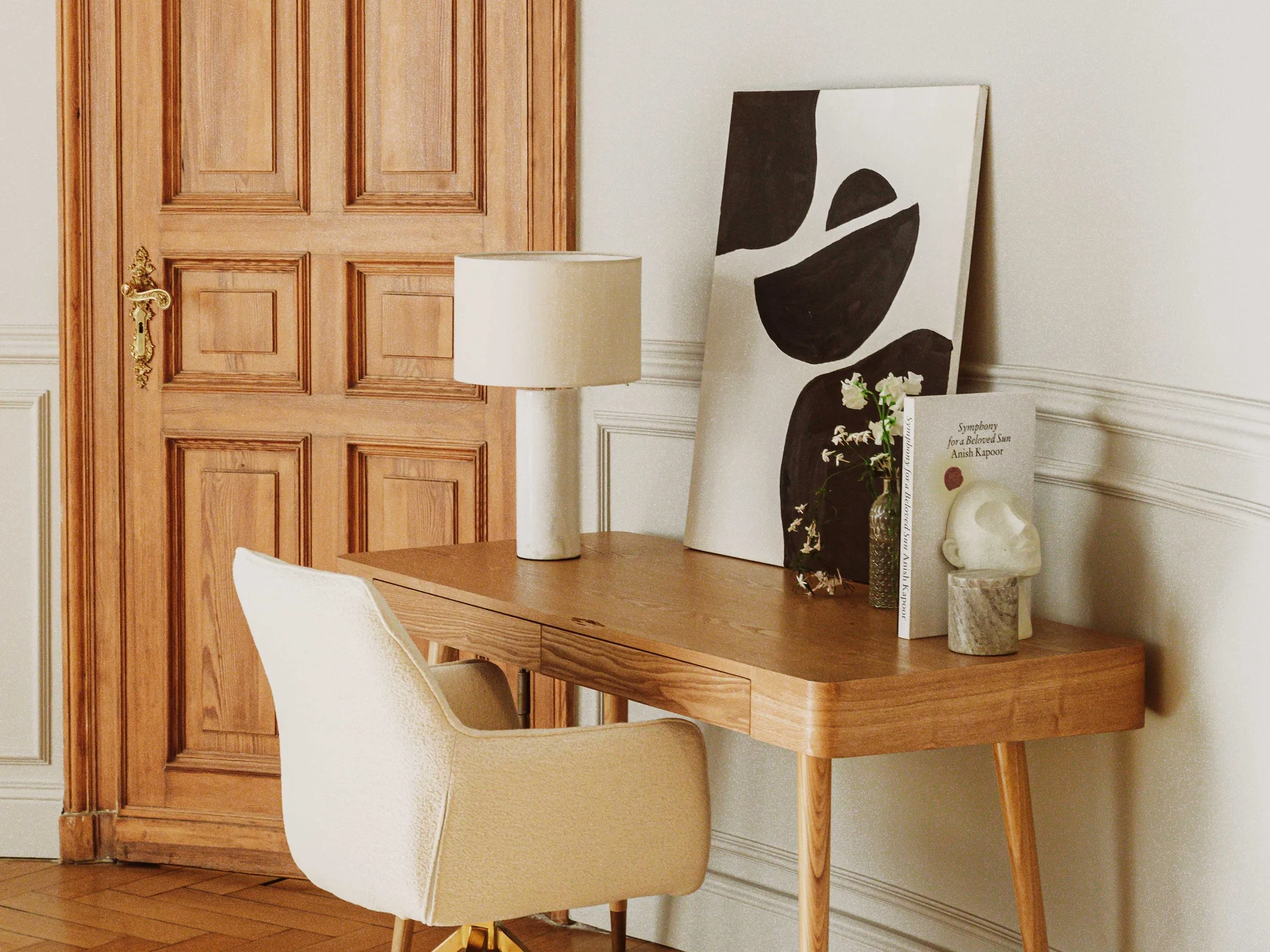 Bureau de chêne clair et chaise ivoire devant une porte ancienne, parquet à bâtons rompus