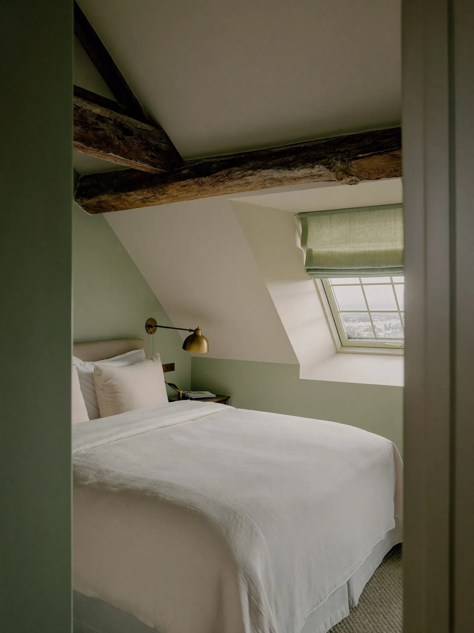 Chambre mansardée sous poutres anciennes, literie blanche et lucarne