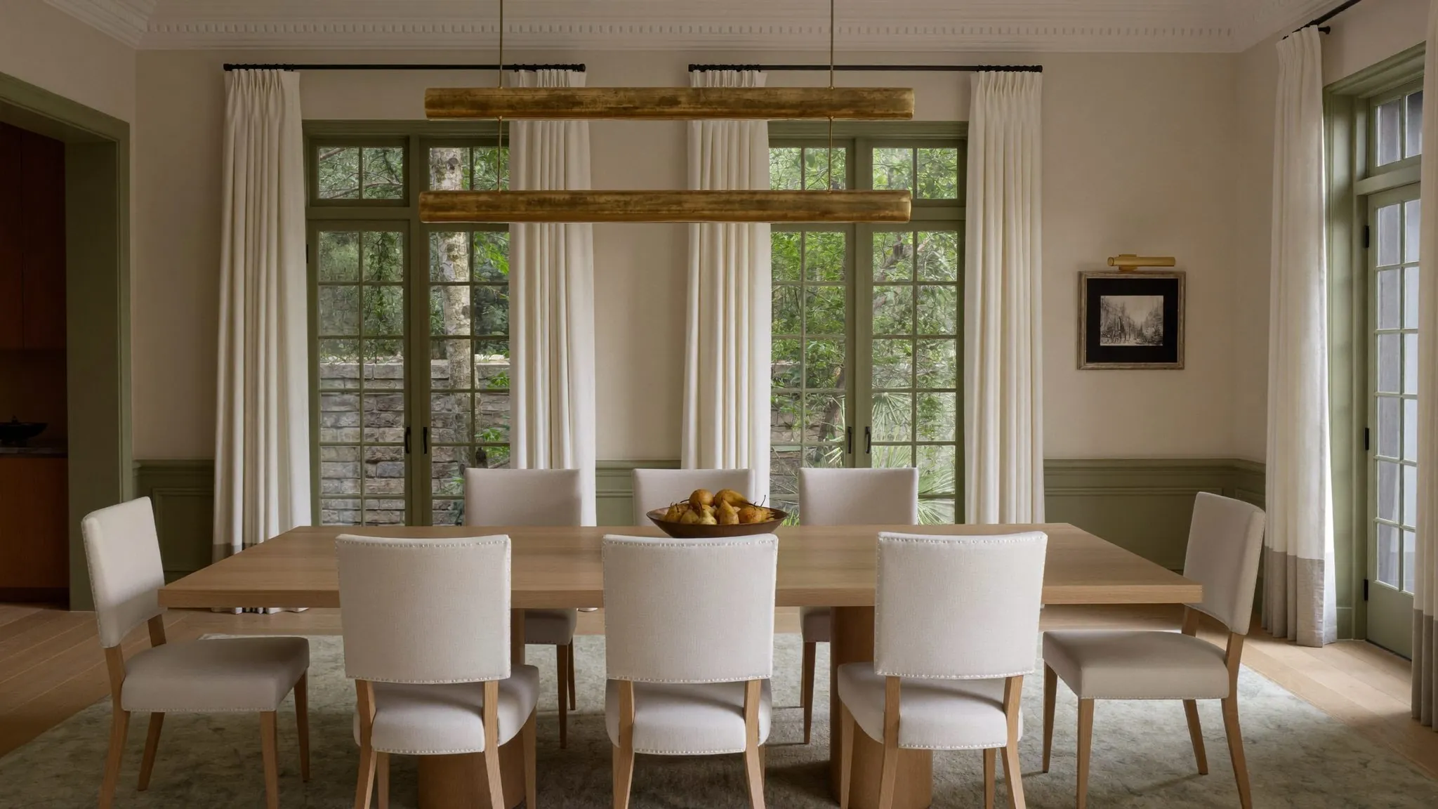 Salle à manger raffinée, longue table de chêne et chaises ivoire sous de hautes fenêtres