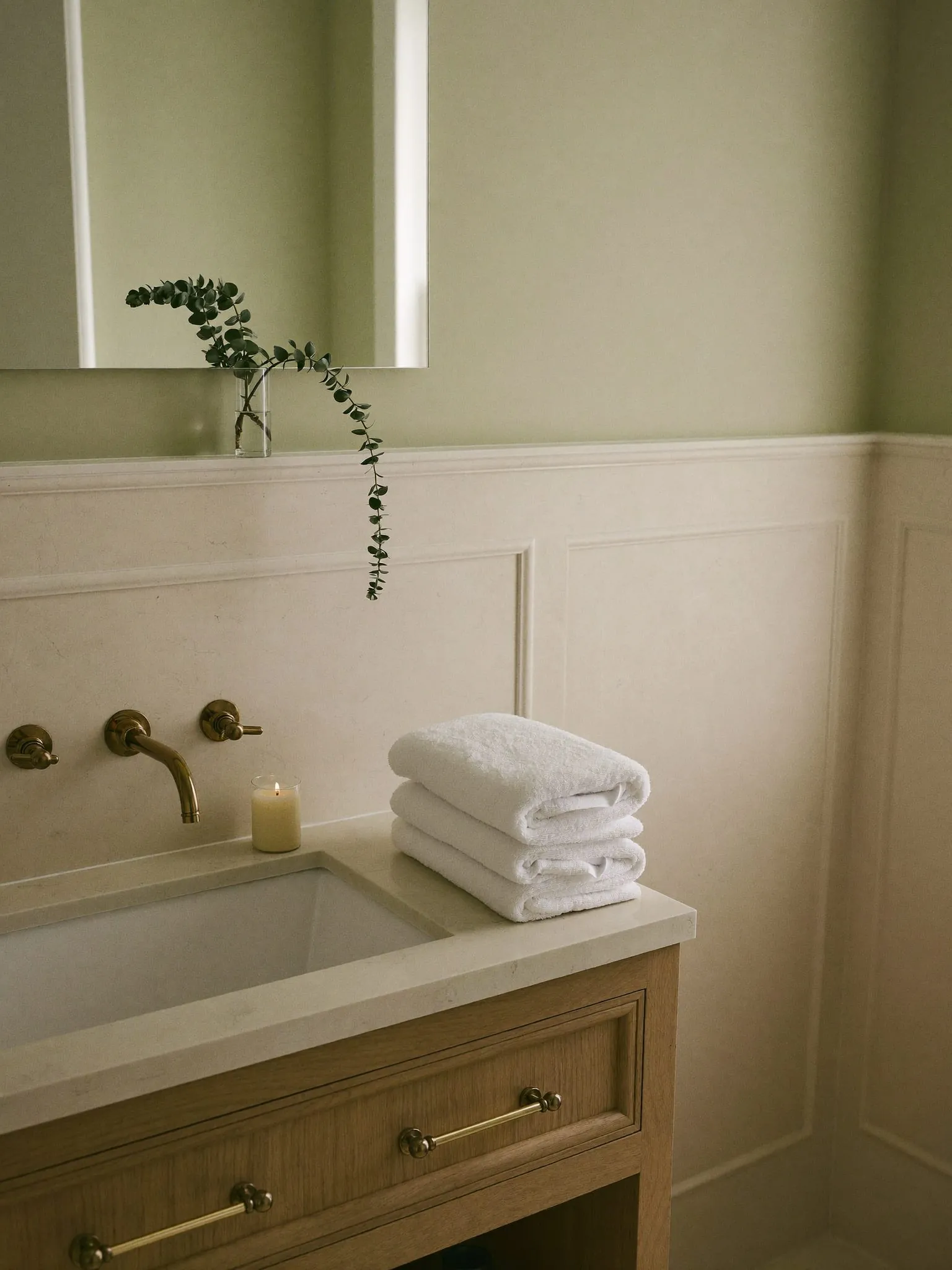 Salle de bains en pierre pâle et chêne, serviettes blanches pliées et eucalyptus