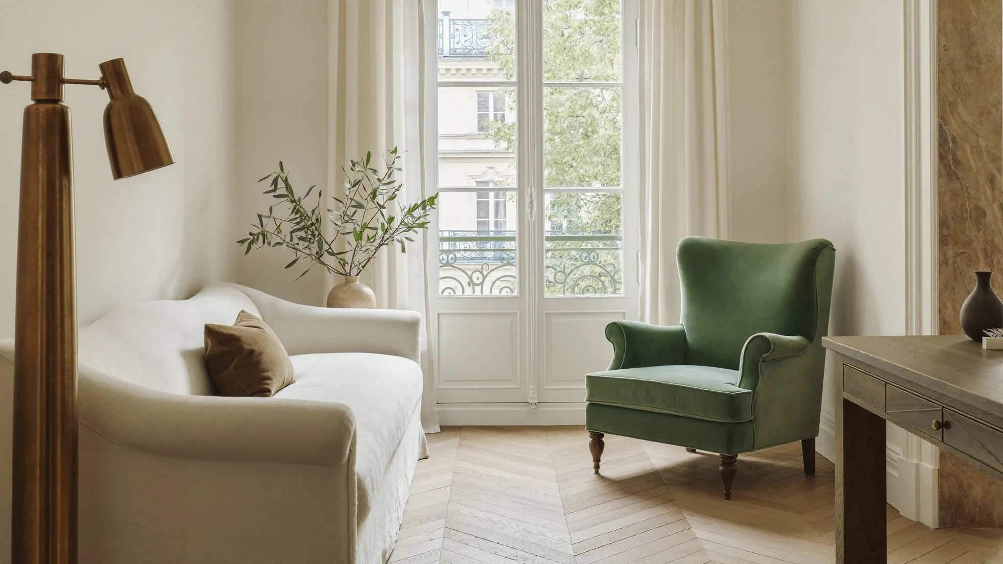 Salon ivoire et sauge, canapé de lin, fauteuil de velours et haute fenêtre voilée de lumière douce