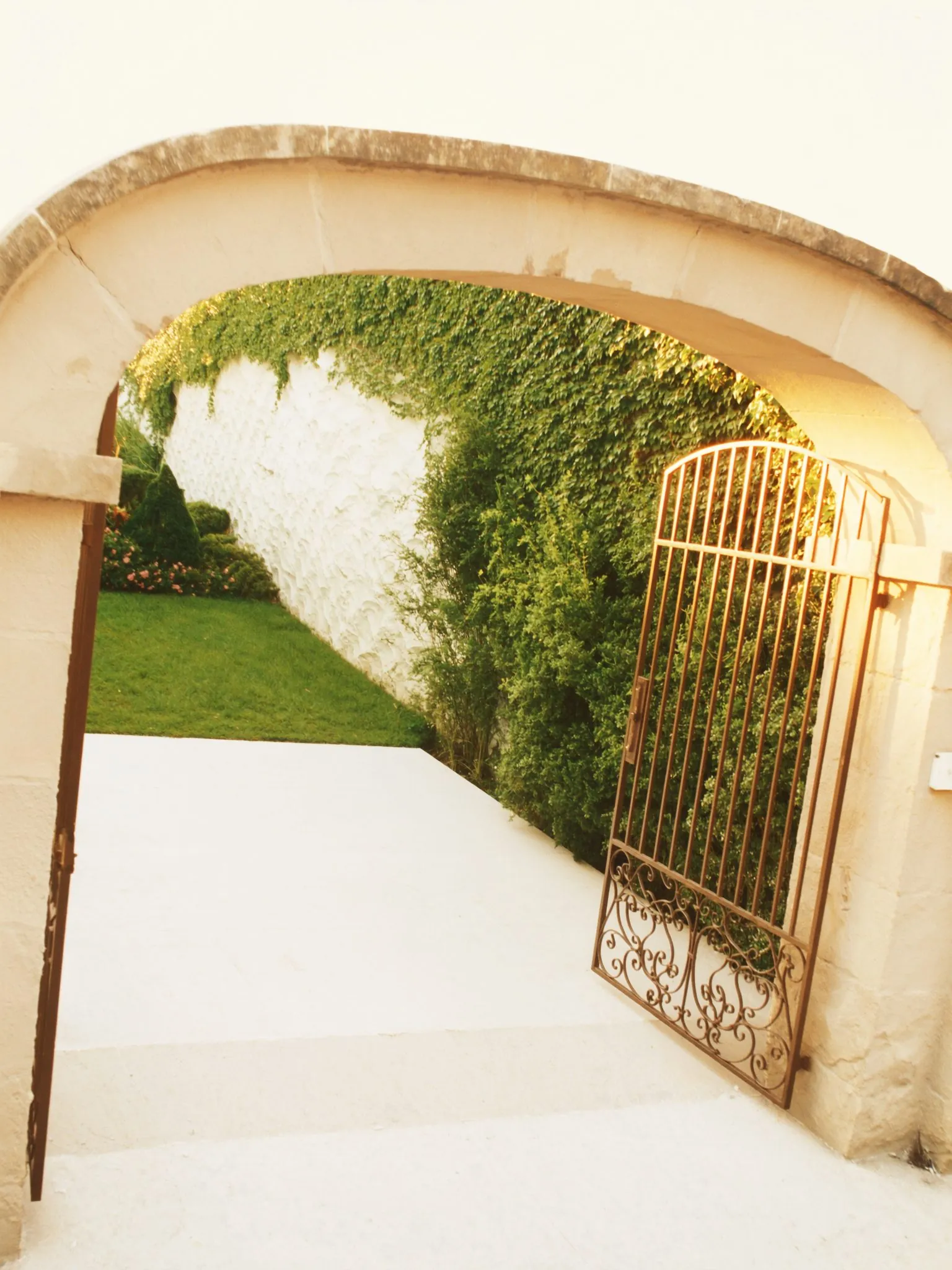 Arche de pierre ouvrant sur un jardin privé, grille de ferronnerie fine entrouverte
